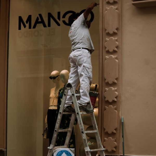 Worker on a ladder renovating the facade of a storefront, enhancing store aesthetics.