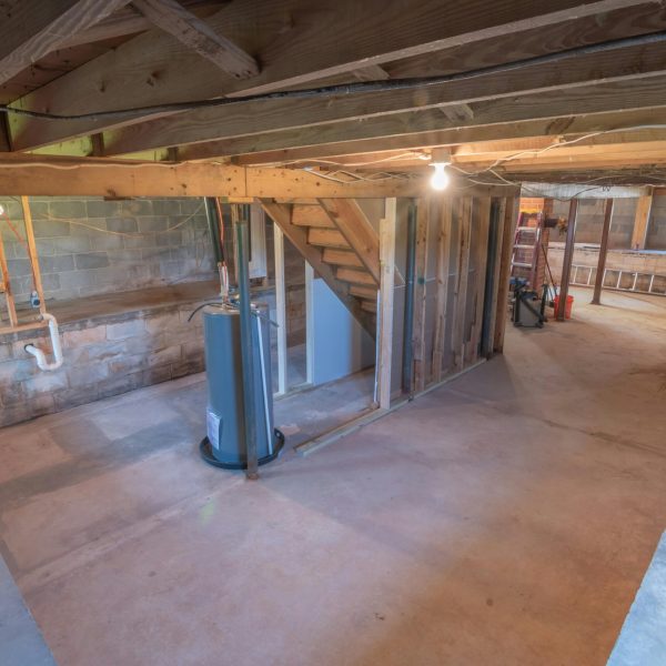 Empty basement with exposed beams and plumbing pipes, ideal for renovation.