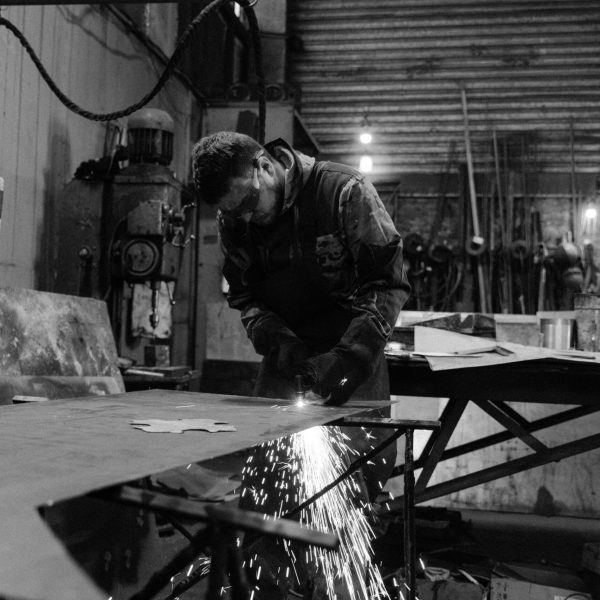 A skilled worker welding metal in an industrial factory setting, in black and white.
